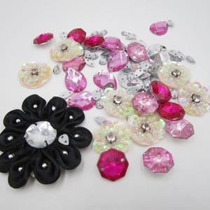 Könnte beinhalten: Sortiment aus rosa, weißen und silbernen Verzierungen, darunter Strasssteine, Pailletten und Stoffblumen. Die Verzierungen sind auf einer weißen Oberfläche verstreut.