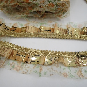 Könnte beinhalten: Nahaufnahme einer dekorativen Borte mit goldfarbenem Metallrand und Rüschendesign. Die Borte zeigt einen Vintage-Zeitungsdruck mit goldenen Akzenten und eine zarte florale Netzunterlage.