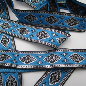Könnte beinhalten: Blauer und schwarzer Besatz mit silbernen Akzenten. Der Besatz zeigt ein sich wiederholendes Muster aus stilisierten Blumen und Diamanten.