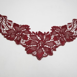 Könnte beinhalten: Eine bordeauxfarbene Spitzenapplikation mit floralem Design. Die Applikation in V-Ausschnitt-Form weist detaillierte Blumenmuster und Durchbrucharbeiten auf. Die Spitze hat einen tiefroten Farbton und eignet sich für verschiedene Bastelprojekte.