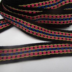 Könnte beinhalten: Schwarzes gewebtes Band mit rosa, blauen und gelben Streifen. Das Band hat ein geometrisches Muster.