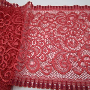 Könnte beinhalten: Nahaufnahme einer Rolle roter Spitzenstoff. Die Spitze weist ein Blumen- und Wirbelmuster mit einem gewellten Rand auf. Der Stoff hat eine tiefe, satte rote Farbe, und das komplizierte Design ist sichtbar.