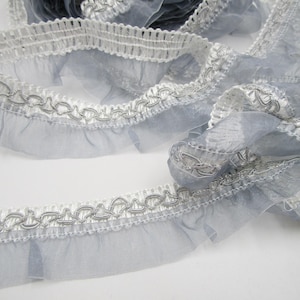 Könnte beinhalten: Grauer und weißer Rüschenbesatz mit einem silbernen Kettenmuster. Der Besatz ist aus einem durchsichtigen Stoff gefertigt und hat einen zarten, femininen Look.