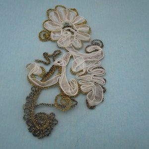 Könnte beinhalten: Eine weiße und goldene Spitzenapplikation mit einem floralen Design. Die Spitze ist zart und filigran, mit einem wirbelnden Muster. Die Applikation ist perfekt, um jedem Projekt einen Hauch von Eleganz zu verleihen.