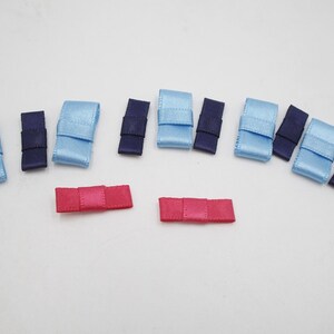 Könnte beinhalten: Eine Auswahl an kleinen Schleifen aus Satinband in verschiedenen Farben. Die Schleifen sind in Hellblau, Marineblau und Rosa gehalten. Die Schleifen sind auf einer weißen Oberfläche angeordnet.