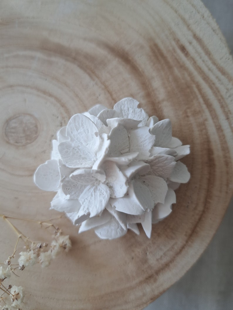 May include: A white ceramic flower with a delicate, layered design. The flower is sitting on a wooden surface.