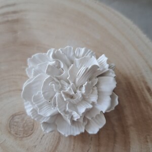 May include: A white ceramic flower with a ruffled texture. The flower is on a light brown wooden surface.