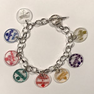 Peut inclure: Un bracelet à breloques en argent avec des breloques en plastique transparent comportant divers mots et expressions, notamment "Divine", "Choice & Accountability", "Integrity", "Knowledge", "Good Works", "Individual", et "Divine", "Virtue".