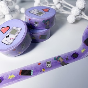 Puede incluir: Cinta washi morada con un patrón repetido de personajes de videojuegos, corazones y el texto "Insertar moneda para continuar".