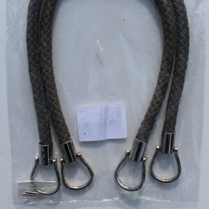 Könnte beinhalten: Geflochtene, graue Handtaschengriffe mit silberfarbenen Metallbeschlägen. Die Griffe befinden sich in einer transparenten Kunststoffverpackung. Die Verpackung trägt den Text "Manici per Borse" und "Bag Handles".