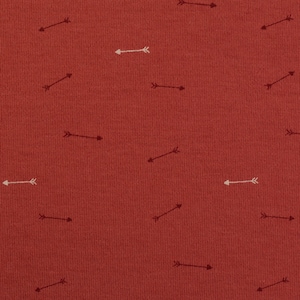Op de afbeelding: Rode stof met een herhalend patroon van witte en zwarte pijlen die in verschillende richtingen wijzen.