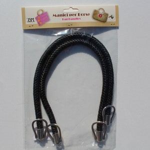 Könnte beinhalten: Zwei schwarze Seil-Taschenhenkel mit silbernen Metallverschlüssen. Die Henkel sind in einer durchsichtigen Plastiktüte verpackt, die ein weißes und braunes Etikett mit der Aufschrift "Manici per Borse" und "Bag Handles" trägt.