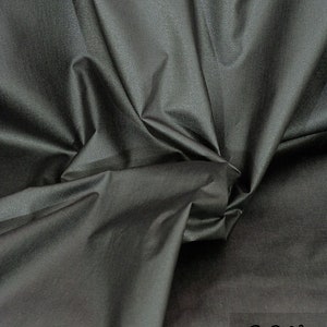 Könnte beinhalten: Nahaufnahme eines dunkelgrauen Stoffes mit dezentem Glanz. Der Stoff ist gefaltet und drapiert, wodurch seine Textur und sein Fall zur Geltung kommen. Der Text "G&N Atelier" ist in der unteren rechten Ecke sichtbar.