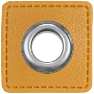 May include: A square, yellow leather eyelet with a silver metal grommet. The eyelet is stitched around the edges with a contrasting thread. The grommet has a smooth, shiny finish and a large, open center.