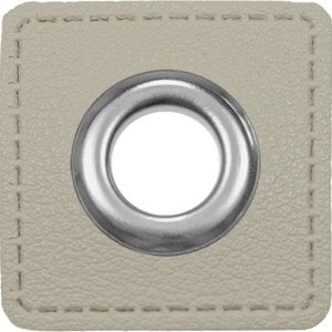 May include: A close-up of a beige fabric square with a silver metal grommet in the center. The grommet has a smooth, shiny finish and a circular hole in the middle.