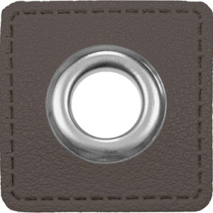 Puede incluir: Un ojal de cuero marrón con un anillo de metal plateado. El ojal está cosido en el cuero con una puntada decorativa.