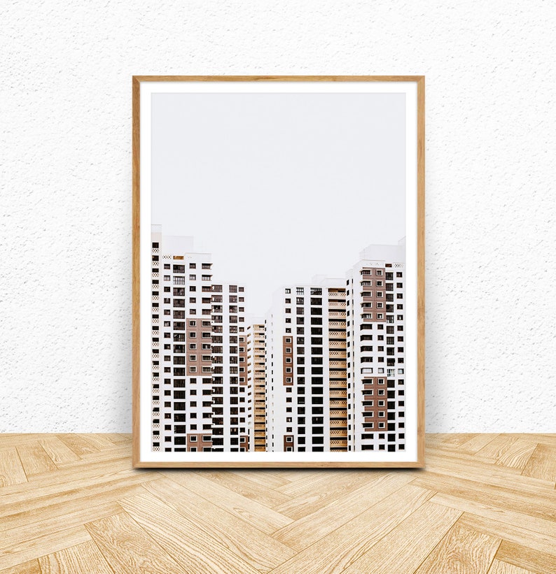 May include: A framed print featuring a minimalist architectural photograph. The image showcases several high-rise apartment buildings with white facades and brown accents. The buildings are set against a plain, light-colored background.