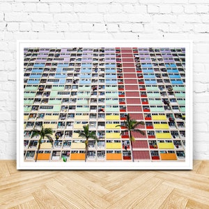 Op de afbeelding: Een kleurrijk appartementencomplex met een kleurenschema van rood, geel, groen, blauw en paars. Het gebouw heeft veel ramen en balkons. Er staan palmbomen voor het gebouw.