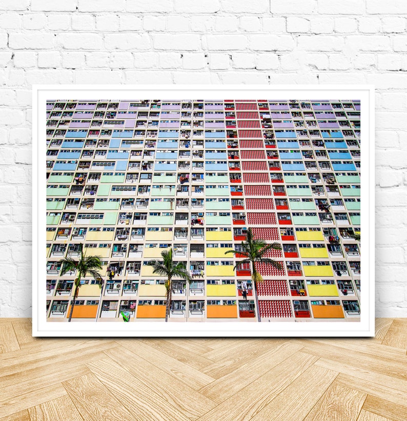 Op de afbeelding: Een kleurrijk appartementencomplex met een kleurenschema van rood, geel, groen, blauw en paars. Het gebouw heeft veel ramen en balkons. Er staan palmbomen voor het gebouw.