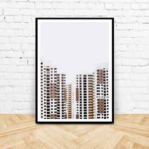 May include: Framed art print featuring a minimalist architectural photograph. The image showcases several high-rise apartment buildings with white and brown facades against a pale sky. The buildings have many windows and balconies. The print is in a black frame.