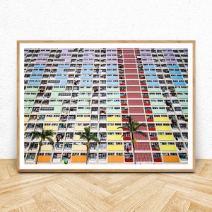 Op de afbeelding: Een kleurrijk appartementencomplex in Hongkong met een herhalend patroon van ramen en balkons. Het gebouw is geschilderd in tinten groen, blauw, geel, oranje en rood. Palmbomen staan voor het gebouw.