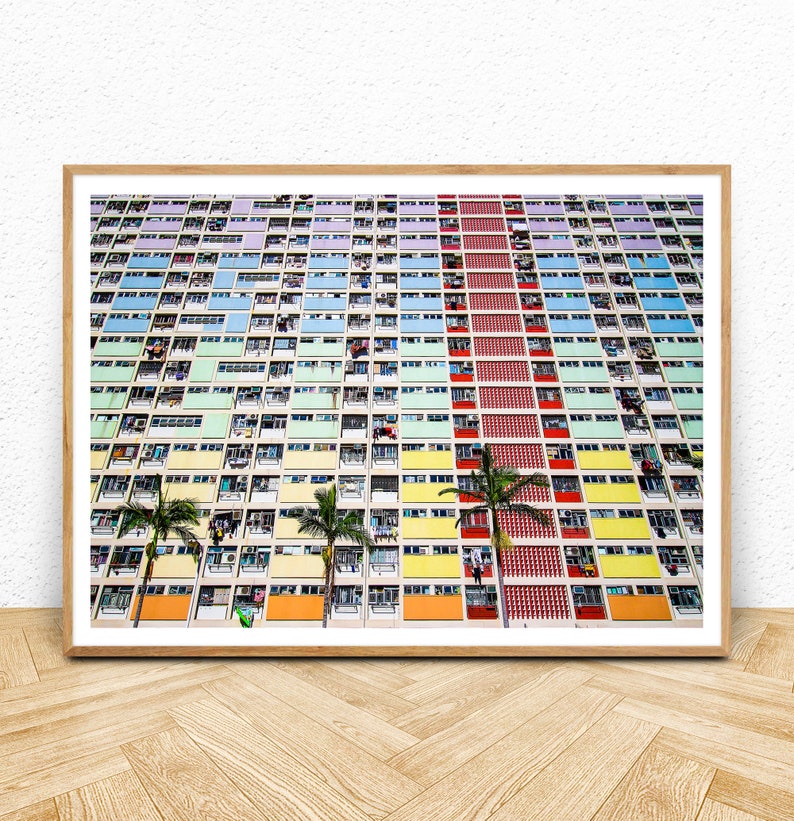 Op de afbeelding: Een kleurrijk appartementencomplex in Hongkong met een herhalend patroon van ramen en balkons. Het gebouw is geschilderd in tinten groen, blauw, geel, oranje en rood. Palmbomen staan voor het gebouw.