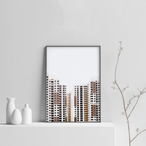 May include: Framed art print featuring a minimalist architectural photograph of several high-rise buildings. The buildings have white and brown facades with numerous windows. The print is in a black frame and is displayed on a white shelf.