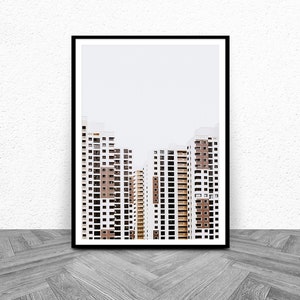 May include: Framed print featuring a minimalist architectural photograph. The image showcases several high-rise apartment buildings with white and brown facades, and numerous windows. The buildings are set against a plain, light-colored sky. The print is in a black frame.