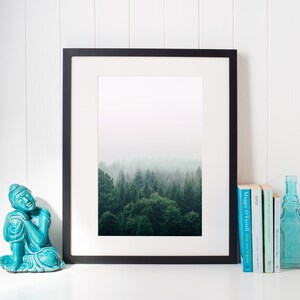 K&ouml;nnte beinhalten: Ein gerahmtes Schwarzwei&szlig;foto eines nebligen Waldes mit einer t&uuml;rkisfarbenen Buddha-Statue und einem Stapel B&uuml;cher auf einer wei&szlig;en Oberfl&auml;che.