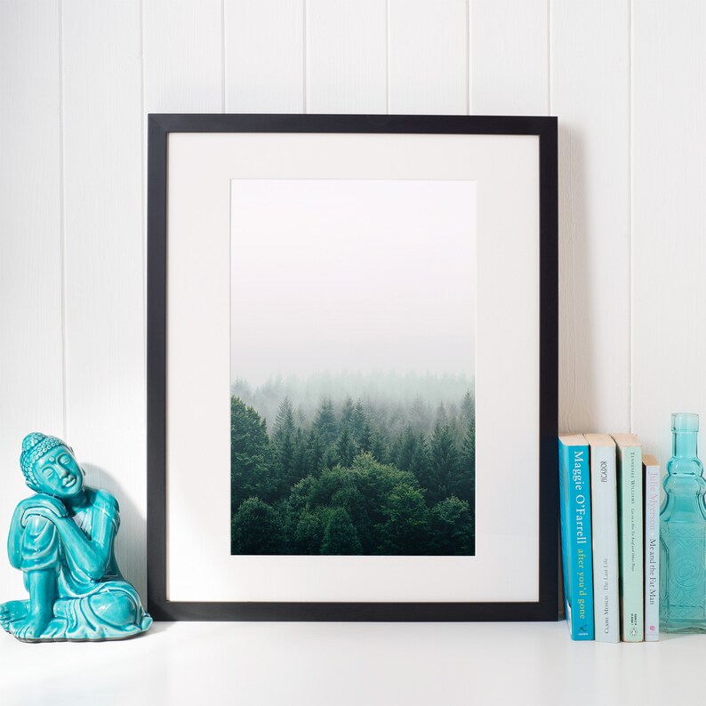 K&ouml;nnte beinhalten: Ein gerahmtes Schwarzwei&szlig;foto eines nebligen Waldes mit einer t&uuml;rkisfarbenen Buddha-Statue und einem Stapel B&uuml;cher auf einer wei&szlig;en Oberfl&auml;che.