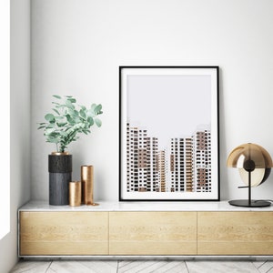 May include: A framed art print featuring a minimalist architectural photograph of high-rise buildings. The print is displayed above a wooden cabinet with decorative vases and a modern lamp. The color palette includes white, brown, and black.