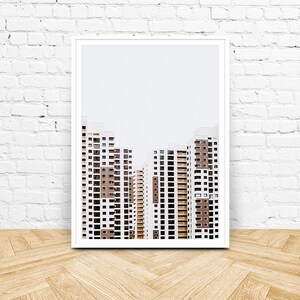 May include: A framed print featuring a minimalist architectural design. The artwork showcases several high-rise buildings with white exteriors, brown accents, and numerous windows. The buildings are set against a pale gray sky.