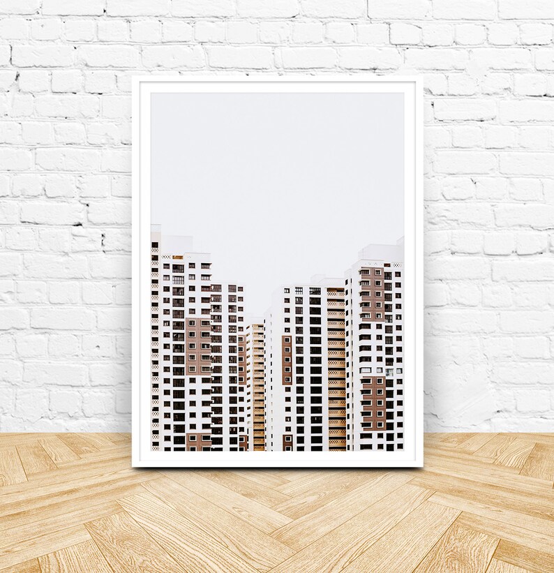 May include: A framed print featuring a minimalist architectural design. The artwork showcases several high-rise buildings with white exteriors, brown accents, and numerous windows. The buildings are set against a pale gray sky.