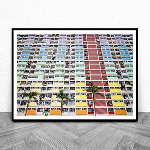 Op de afbeelding: Een kleurrijk appartementencomplex in Hongkong met een verscheidenheid aan pastelkleuren, waaronder blauw, groen, geel en oranje. Palmbomen staan voor het gebouw.