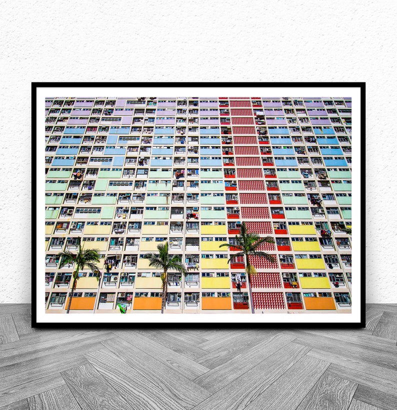 Op de afbeelding: Een kleurrijk appartementencomplex in Hongkong met een verscheidenheid aan pastelkleuren, waaronder blauw, groen, geel en oranje. Palmbomen staan voor het gebouw.