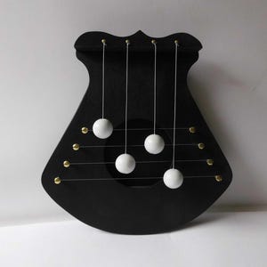 Può includere: Uno strumento musicale in legno nero con cinque sfere bianche appese a delle corde. Lo strumento ha una forma arrotondata e un foro al centro.