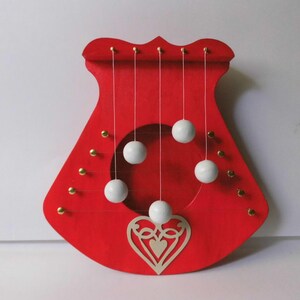 May include: A red decorative wall hanging with a heart-shaped cutout and gold accents. White spheres are suspended from the top, creating a unique visual effect. The design is symmetrical and eye-catching.