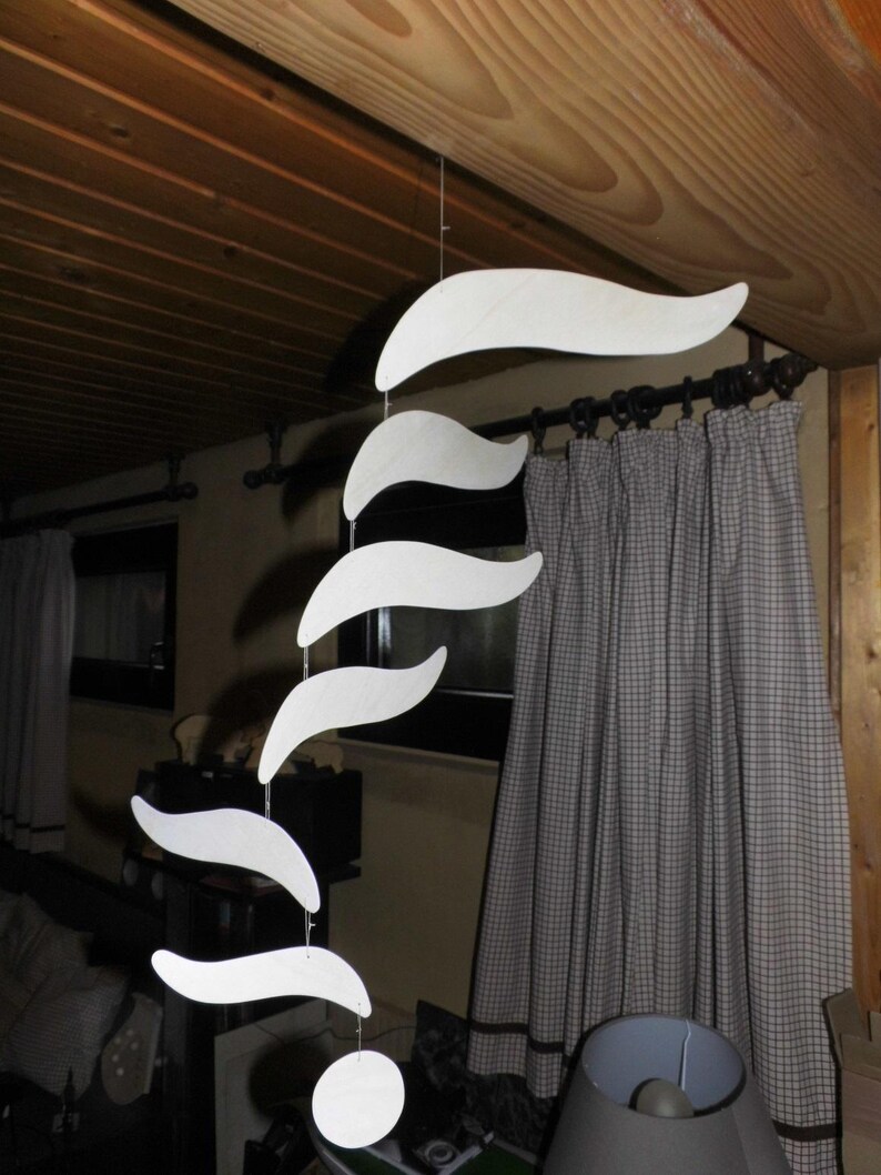 Puede incluir: M&oacute;vil de madera blanca con una serie de formas curvas, similares a olas, suspendidas de un hilo. El m&oacute;vil cuelga de un techo de madera, con una cortina de tonos neutros en el fondo. Las formas var&iacute;an en tama&ntilde;o, creando una pieza decorativa.