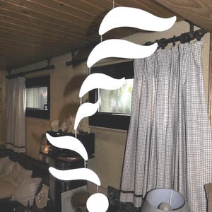 Puede incluir: Un m&oacute;vil colgante blanco moderno con una serie de formas curvas en forma de hoja suspendidas de un alambre fino. Una esfera blanca en la parte inferior. El m&oacute;vil cuelga frente a una ventana con cortinas a cuadros.