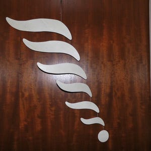 Puede incluir: M&oacute;vil abstracto con una serie de formas blancas y curvas suspendidas de un solo punto. Las formas disminuyen de tama&ntilde;o, culminando en un peque&ntilde;o disco redondo. El m&oacute;vil cuelga sobre un fondo de madera marr&oacute;n oscuro.