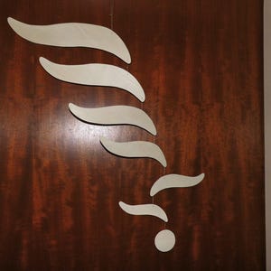 Puede incluir: Un m&oacute;vil moderno y abstracto con una serie de formas de madera curvas de color claro suspendidas de un alambre fino. Las formas caen en cascada sobre un fondo oscuro de vetas de madera, creando una sensaci&oacute;n de movimiento y equilibrio. La forma inferior es un peque&ntilde;o c&iacute;rculo.