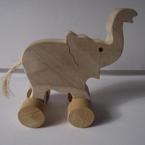 May include: A wooden toy elephant with a long trunk, large ears, and four wheels. The elephant is painted in a natural wood colour and has a small tail made of twine.