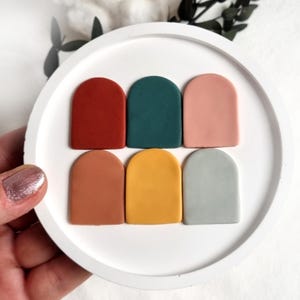 May include: Six small, arched ceramic tiles in various colors, including red, green, pink, orange, yellow, and blue. The tiles are arranged in two rows of three on a white surface.