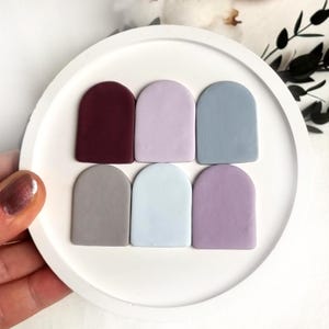 May include: Six small, arched ceramic tiles in various shades of purple, blue, and gray. The tiles are arranged in two rows of three on a white surface.