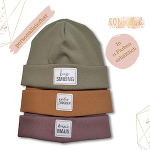 Könnte beinhalten: Drei Beanies mit verschiedenen bestickten Patches. Der oberste Hut ist grün mit einem weißen Patch, auf dem "keep smiling" steht. Der mittlere Hut ist orange mit einem weißen Patch, auf dem "großer bruder" steht. Der unterste Hut ist rosa mit einem weißen Patch, auf dem "mini maus" steht.