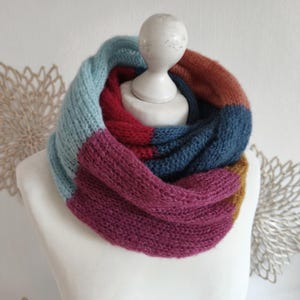 Könnte beinhalten: Ein grob gestrickter Infinity-Schal mit einem Color-Block-Design in den Farben Hellblau, Dunkelrot, Dunkelblau, Magenta und Senfgelb. Der Schal ist in einer gerippten Struktur gefertigt und wird auf einem weißen Schaufensterpuppen-Torso präsentiert.