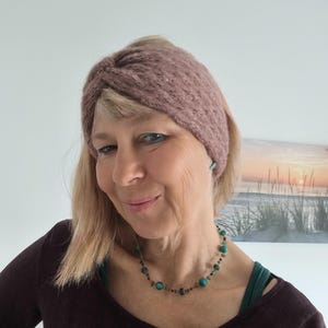 Könnte beinhalten: Ein gestricktes Stirnband in Staubrosa. Die Person trägt eine türkisfarbene Perlenkette und passende Ohrringe. Sie trägt ein dunkelbraunes Langarmshirt.