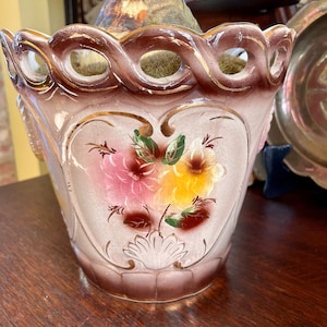 May include: A brown ceramic planter with a gold trim and floral design. The planter has a scalloped rim and a bulb is planted inside.