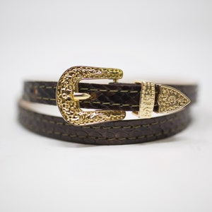 May include: A brown leather belt with a gold-toned buckle. The buckle has a detailed design.