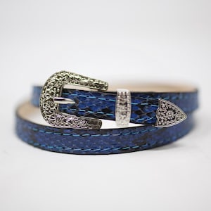 May include: A blue leather belt with a silver buckle. The buckle has a decorative design.